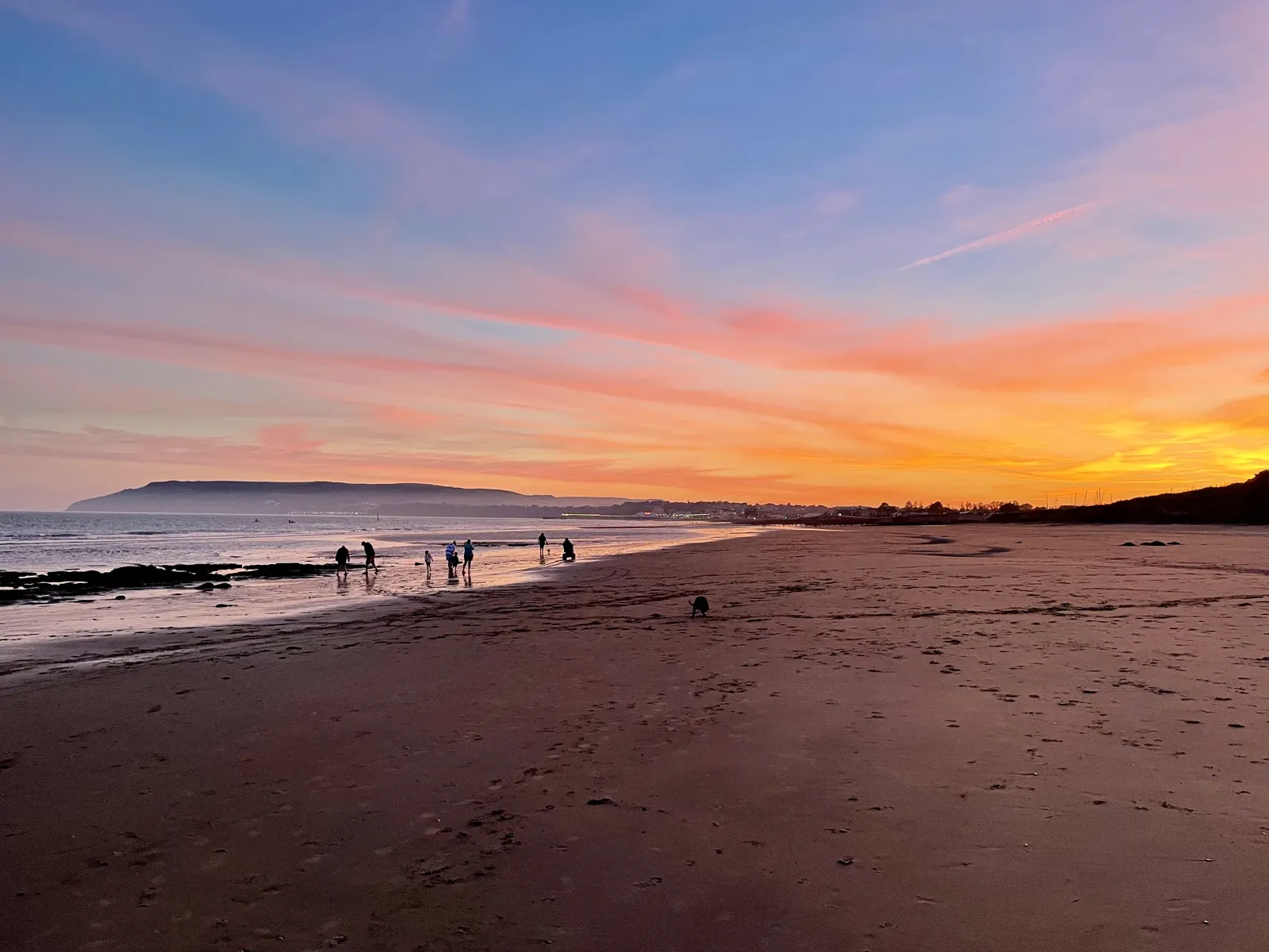 Sunset over Yaverland beach with families walking at the water's edge